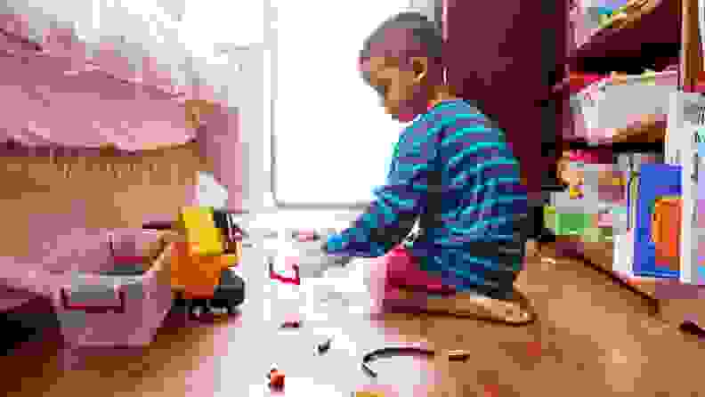 A small child plays with toys on the floor of a bedroom.