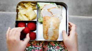 Hands in an open lunch box with food
