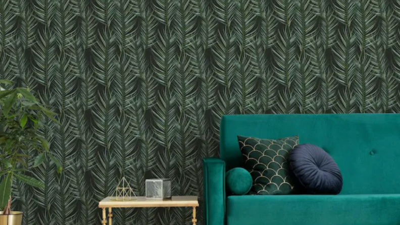 A dark freen leaf print wallpaper is pasted on the walls. A teal couch sits in front of the wallpapered wall.