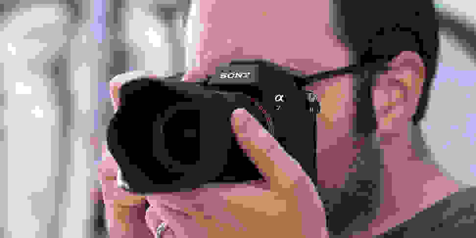 A photographer holds a camera viewfinder up to their eye to compose a shot.