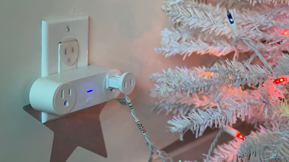 A smart plug plugged into the wall powering an artificial Christmas tree