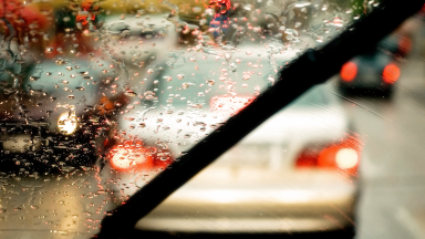 Close-up of a windshield wiper blade clearing away the rain from one side, a painterly cityscape visible beyond the windshield.