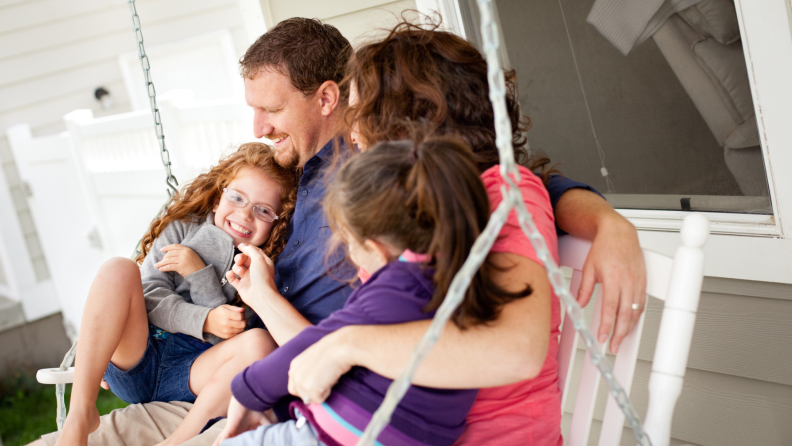 Smiling family of three spending quality time together on white porch swing outdoors