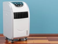 A large white portable air conditioner with wheels stands on a wood floor.
