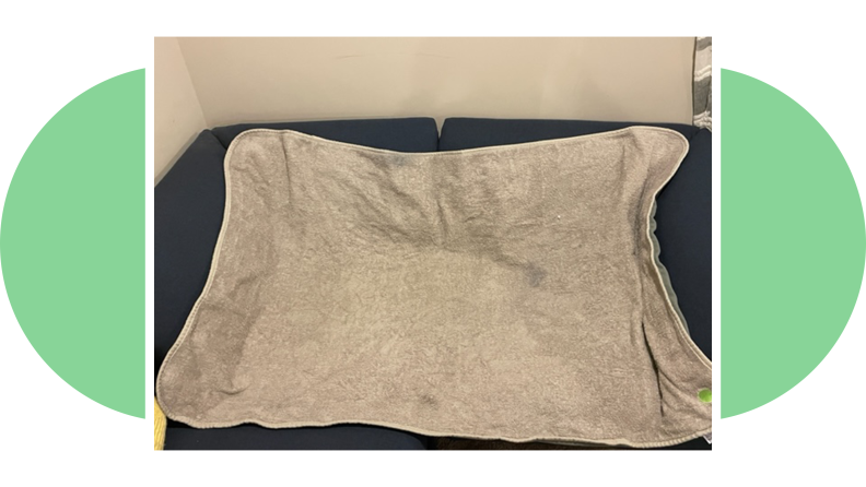 A gray Peapod bedwetting mat on top of navy colored couch in front of wall indoors.