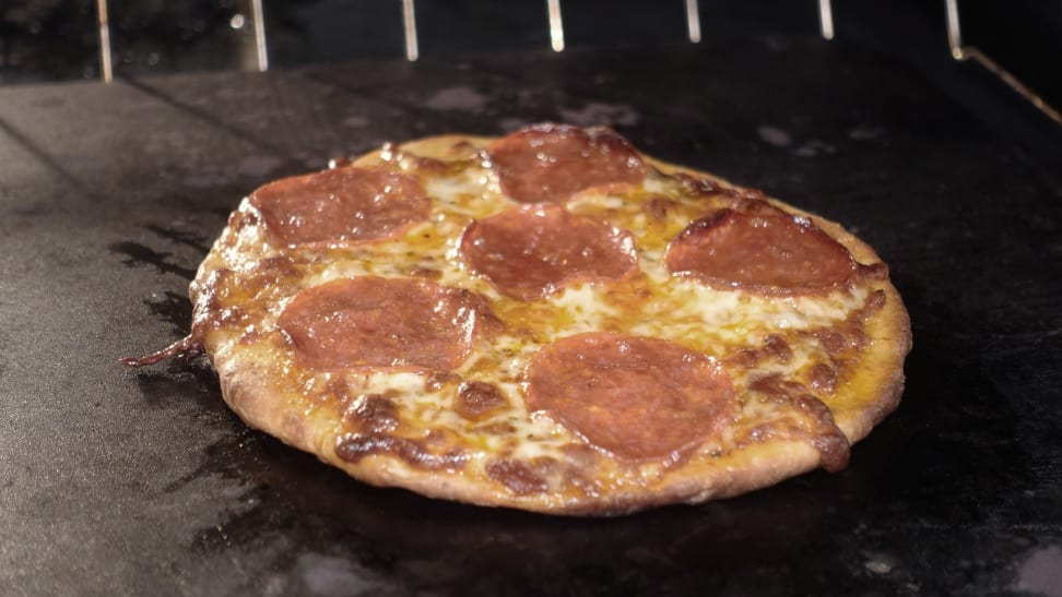 A pepperoni pizza cooking on baking steel in a hot oven.