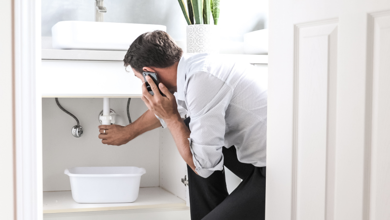 Person looking at leaking piped under sink.