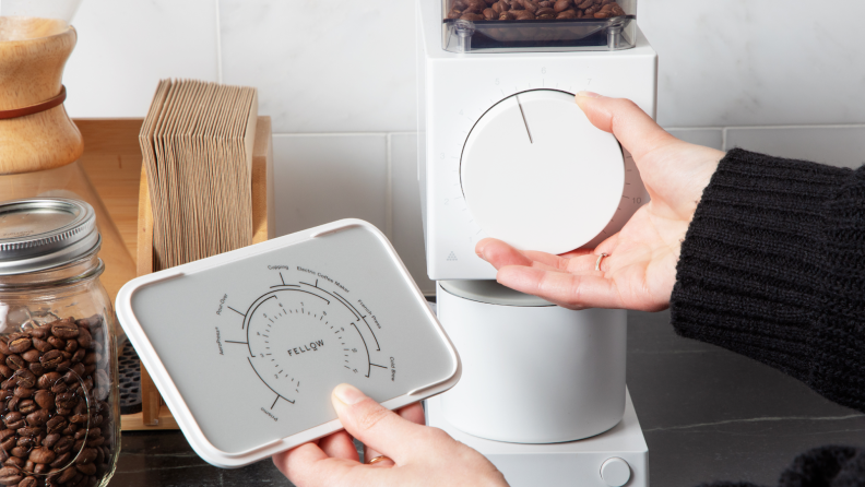 Person adjusting large dial on the Fellow Ode Gen 2 coffee grinder while looking at manual.