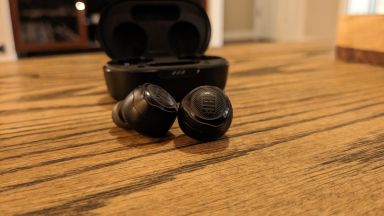 The The JBL Quantum TWS Air earbuds on a wood table.