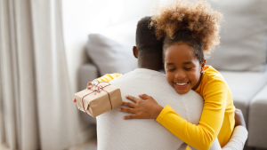 Child smiling while hugging parent with present in hand.