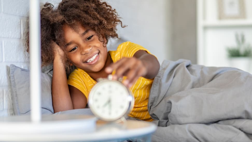 Young girl smiling in bed turning off her alarm clock.