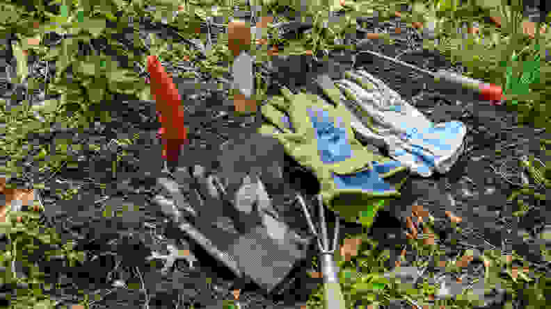 Showa Atlas, Stonebreaker, and West County gardening gloves all lay across some freshly-dug soil in a garden.