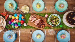A decorated table for Easter dinner with glazed ham, painted eggs, tulips and Easter cake.