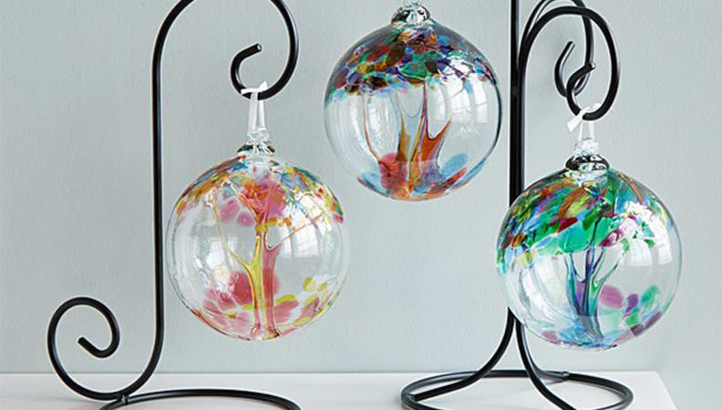 assorted colored glass globes hanging from ironlike stand on grey background.