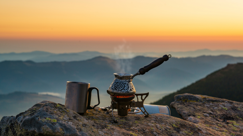 A little Turkish coffee pot is sitting on top of stove against the backdrop of endless mountains.