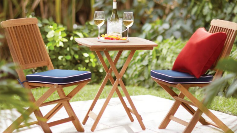 Wooden bistro set with matching blue cushions and one red pillow on a patio