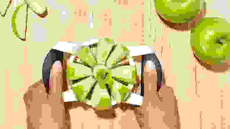 A person slices green apples with a device.
