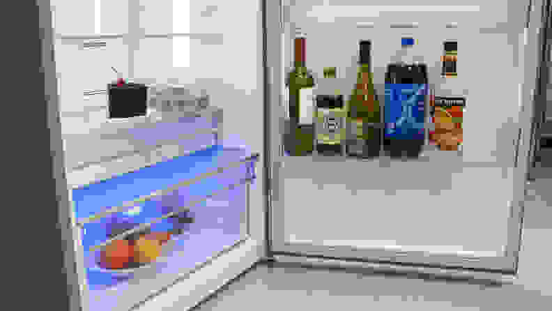A close-up on the bottom half of the fridge compartment and its door. Both the crisper and door bin are stocked with food, and you can see the blue glow coming from its crisper LED.