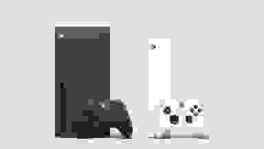 A black Xbox with a black controller in front of it next to a white Xbox with a white controller in front of it.