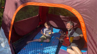 A child, a puppy, and a father recline in a Coleman Skylodge Instant Tent