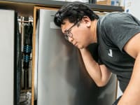 A person crouched down and listening closely to a dishwasher.