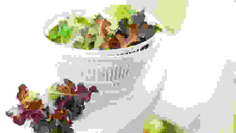 A salad spinner filled with fresh lettuce on a white countertop.