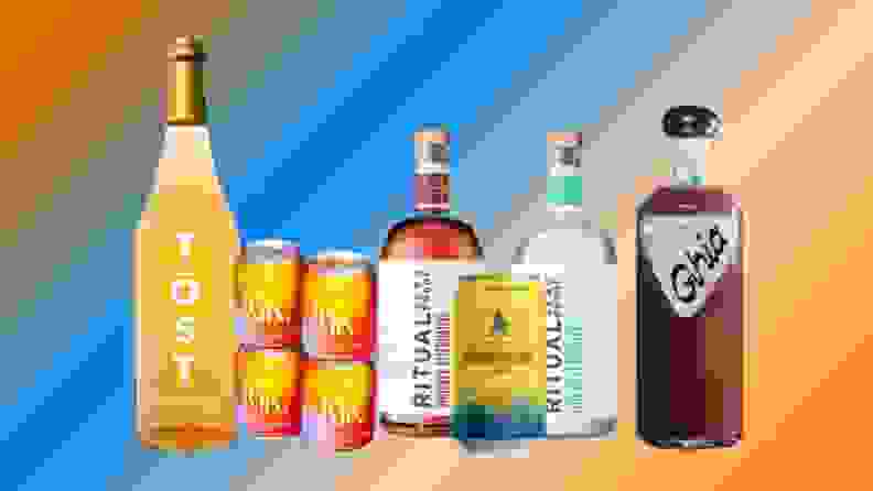 Bottles of several brands of zero-proof cocktail, wine, and liqueur lined up on a colorful, blurry background.