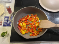 A pan on a stove filled with red bell pepper and bright yellow mango.