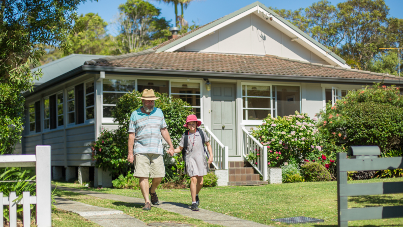 A grandparent and grandchild hold hands while walking outside the home.