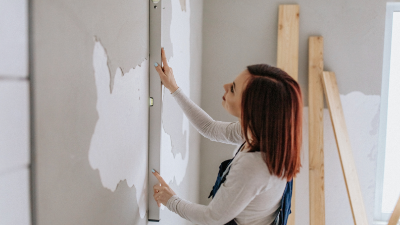 Woman staring at wall to use tool to measure dry wall.