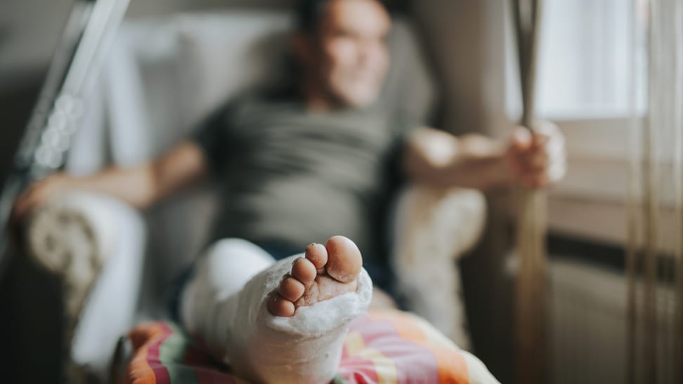 Person looking out window while sitting with injured leg propped up on pillow.