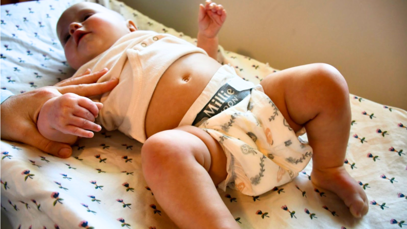 A baby wearing a pair of Millie Moon diapers on a changing table pad.