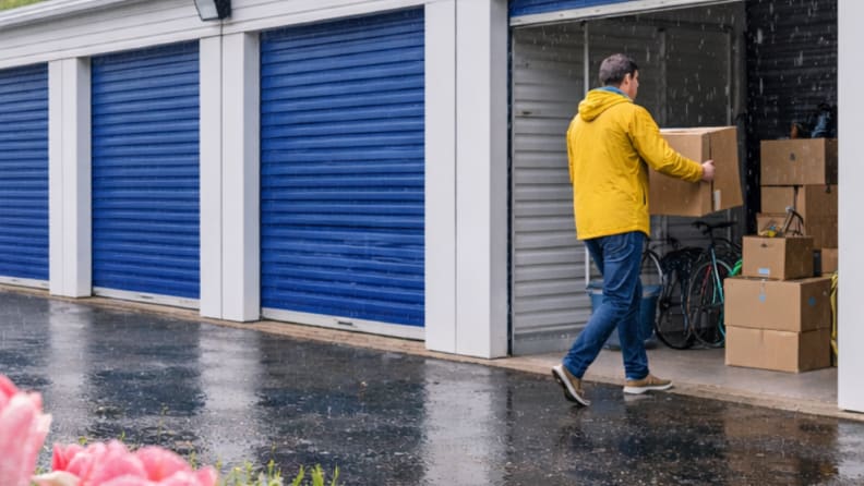Man storing a box in an outdoor self-storage unit during the rain