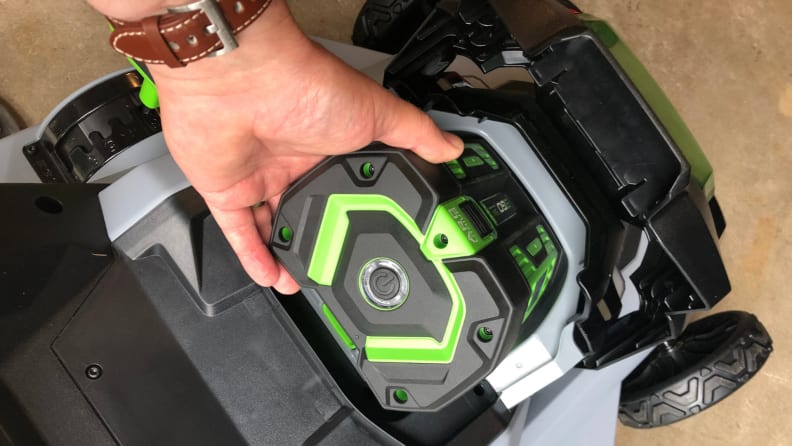 A hand pulls the green Ego Power+ lawn mower battery out of it's spot.
