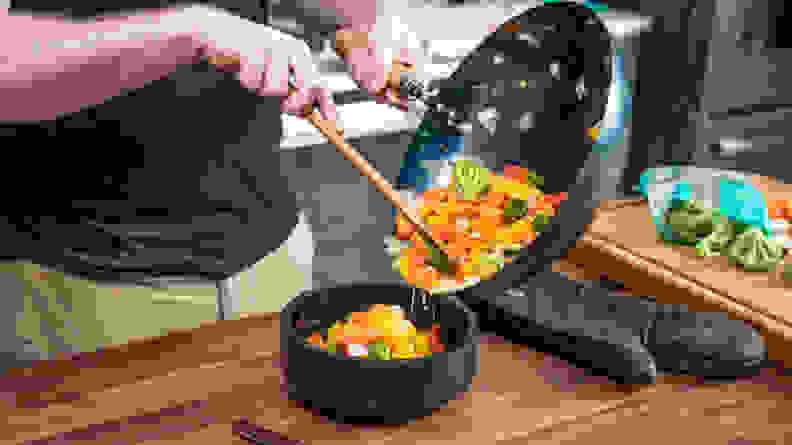 A person is pouring out a medley of vegetables from a wok into a bowl.