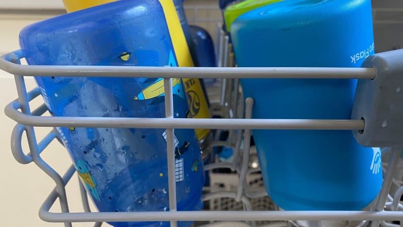 A row of kids' water bottles on the top rack of a dishwasher