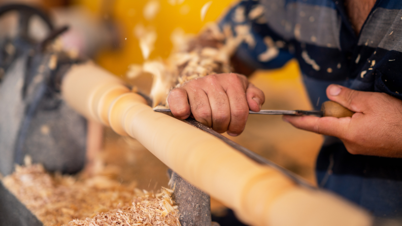 Person creating a wooden baluster with tool.