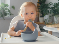 A baby in a high chair licking a spoon.