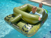 Two children smiling inside of tank-shaped pool inflatable outdoors in pool.