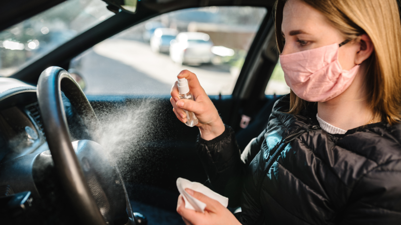 A woman sprays antibacterial sanitizer on her steering wheel.