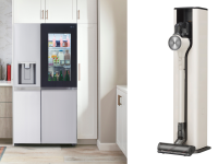 A modern refrigerator has a glass panel and it is opposite a cordless vacuum
