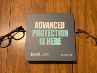 Two pairs of glasses on a wooden surface, along with a box that reads “Advanced protection is here, EyeQLenz Zenni.”