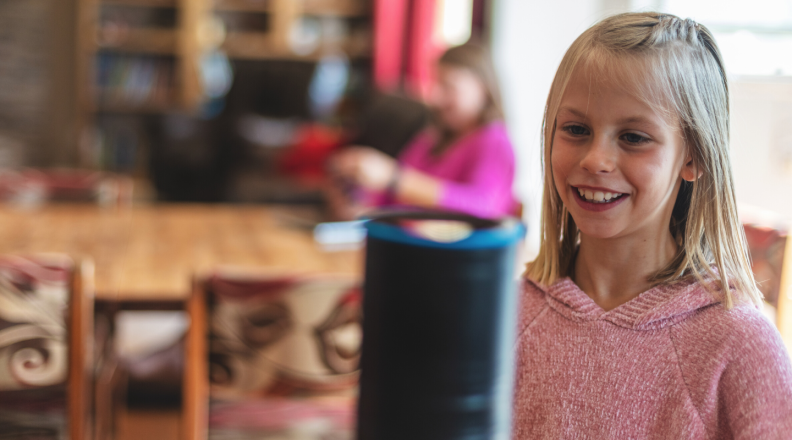 A girl stands in front of a smart speaker.