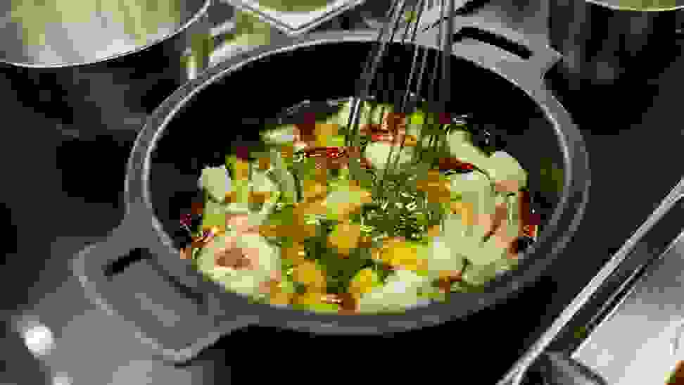 A dish being stirred and cooked in the kitchen of a Spanish restaurant. Green and white vegetables in water or broth.