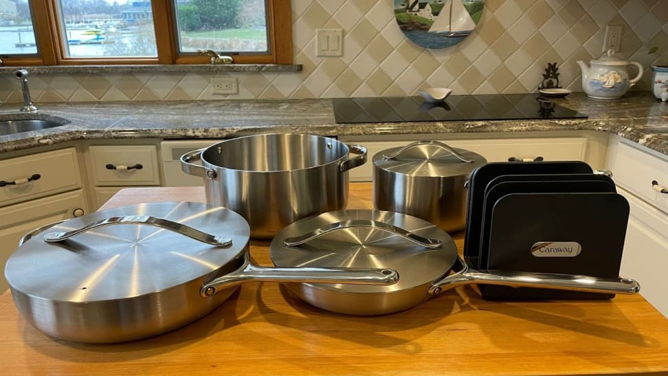 Caraway's stainless steel cookware set sitting on top of wooden island inside of modern kitchen.
