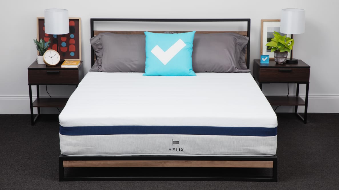 Helix Midnight Mattress without sheets inside of bed frame with three pillows on top, in between two nightstands with lamps and in front of white wall.