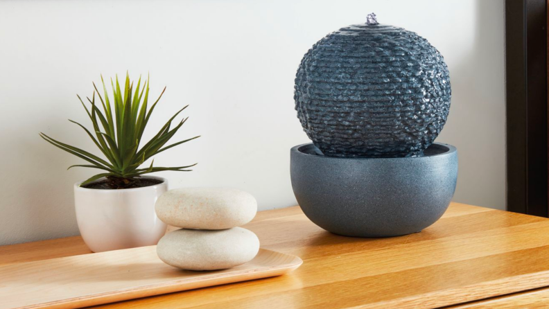 A small ceramic fountain on a table alongside a potted plant.