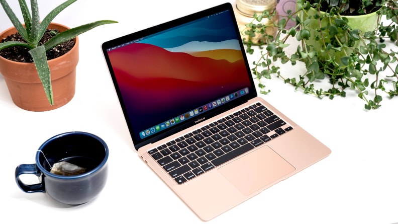 MacBook lies on white table surrounded by plants