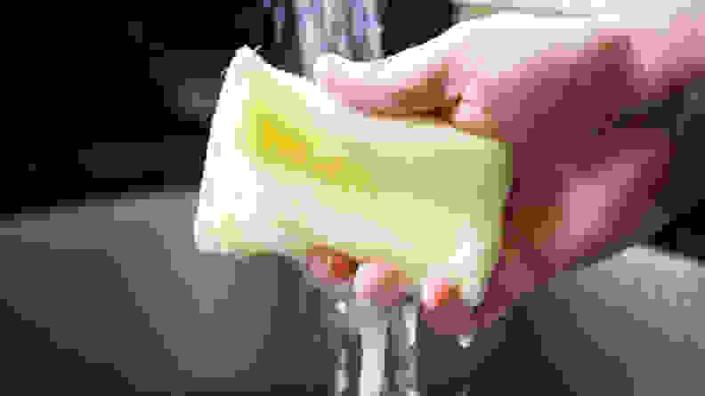 A hand squeezing a Scotch-Brite Dobie sponge in running water