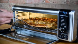 A person uses a spatula to slide a pizza out of the Ninja Foodi Air Fry Oven.